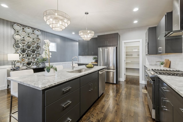 kitchen featuring pendant lighting, a kitchen island with sink, sink, appliances with stainless steel finishes, and a notable chandelier