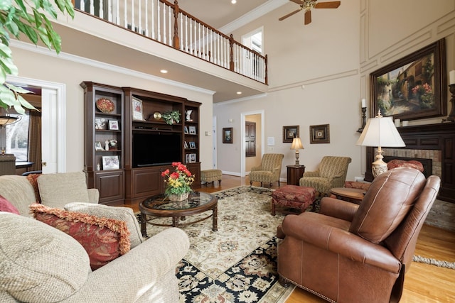 living room with a towering ceiling, light hardwood / wood-style flooring, ornamental molding, and ceiling fan