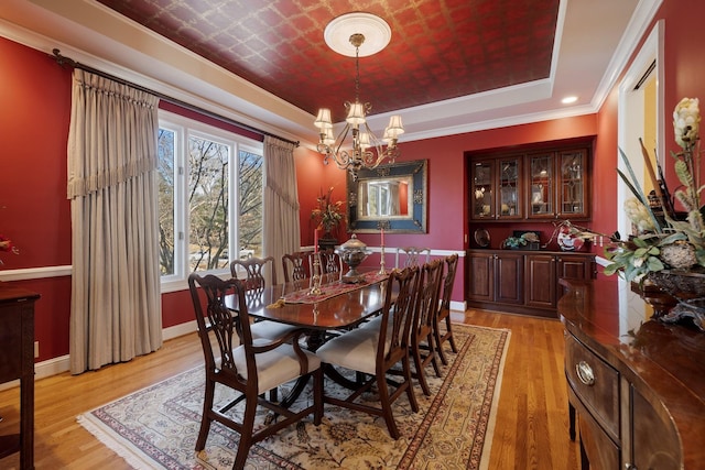 dining space with a notable chandelier, a tray ceiling, light hardwood / wood-style flooring, and ornamental molding