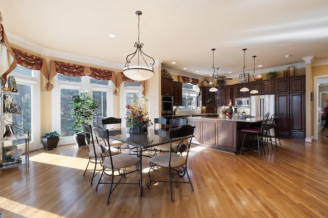 dining space with ornamental molding, sink, and light hardwood / wood-style flooring