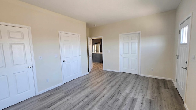 unfurnished bedroom with stainless steel fridge and light hardwood / wood-style flooring