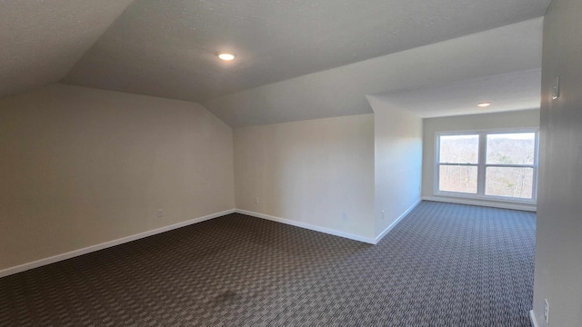 additional living space featuring a textured ceiling, dark colored carpet, and lofted ceiling