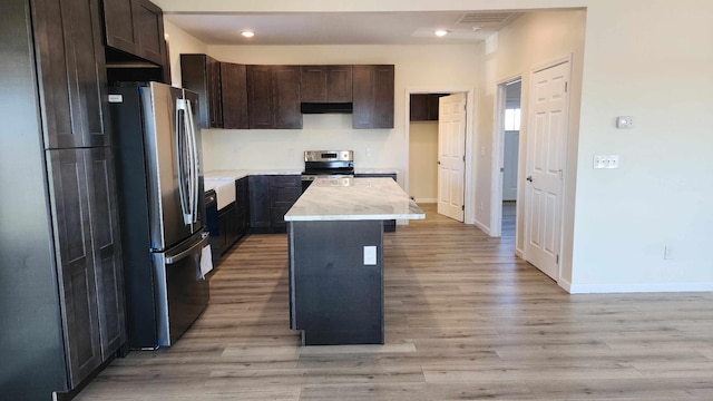 kitchen featuring appliances with stainless steel finishes, a kitchen island, dark brown cabinets, and light wood-type flooring