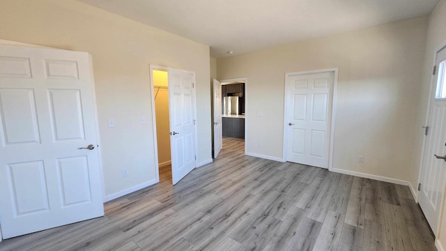 unfurnished bedroom with light hardwood / wood-style floors, a spacious closet, a closet, and stainless steel refrigerator