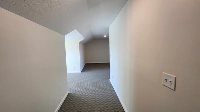 hallway featuring dark carpet, lofted ceiling, and a textured ceiling