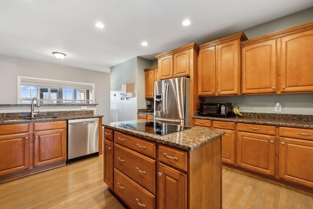 kitchen with stainless steel appliances, sink, light wood-type flooring, dark stone counters, and a center island