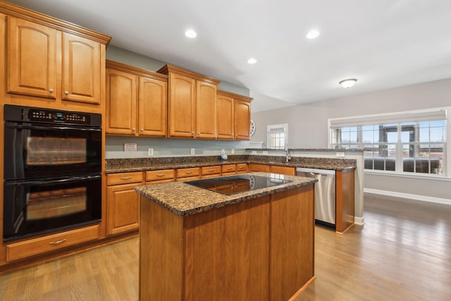 kitchen with black appliances, a kitchen island, dark stone countertops, light hardwood / wood-style floors, and kitchen peninsula