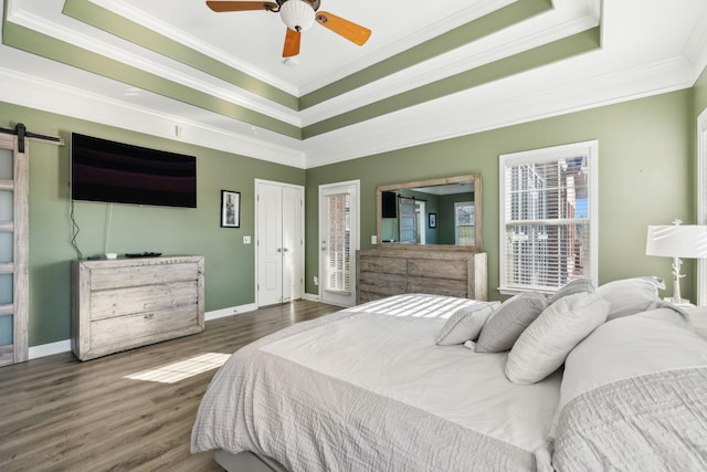 bedroom featuring dark hardwood / wood-style floors, a raised ceiling, ceiling fan, crown molding, and a barn door