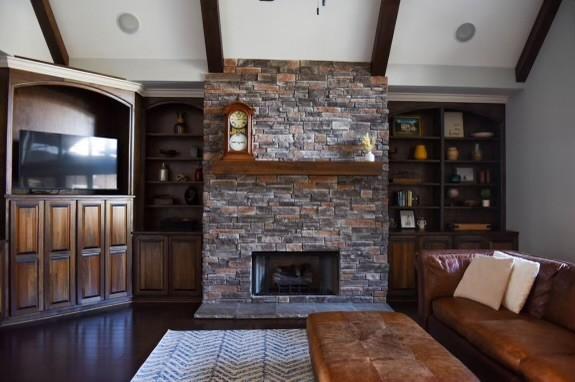 living room with beamed ceiling, a stone fireplace, built in shelves, and dark wood-type flooring