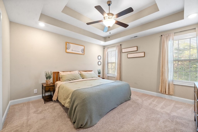 carpeted bedroom featuring ceiling fan, multiple windows, and a tray ceiling