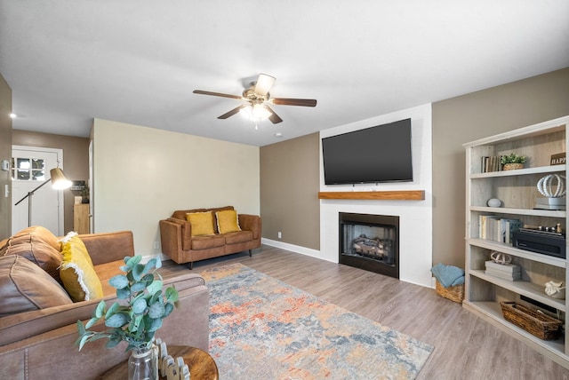 living room featuring ceiling fan, a large fireplace, and light hardwood / wood-style floors