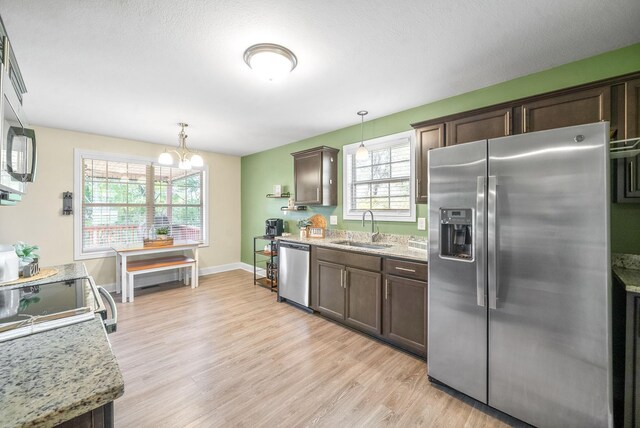 kitchen with light stone countertops, sink, hanging light fixtures, dark brown cabinets, and appliances with stainless steel finishes