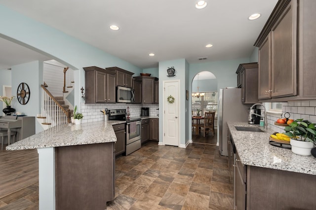 kitchen featuring kitchen peninsula, appliances with stainless steel finishes, dark brown cabinetry, and decorative backsplash