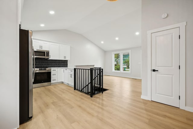 kitchen featuring white cabinets, vaulted ceiling, stainless steel appliances, and tasteful backsplash