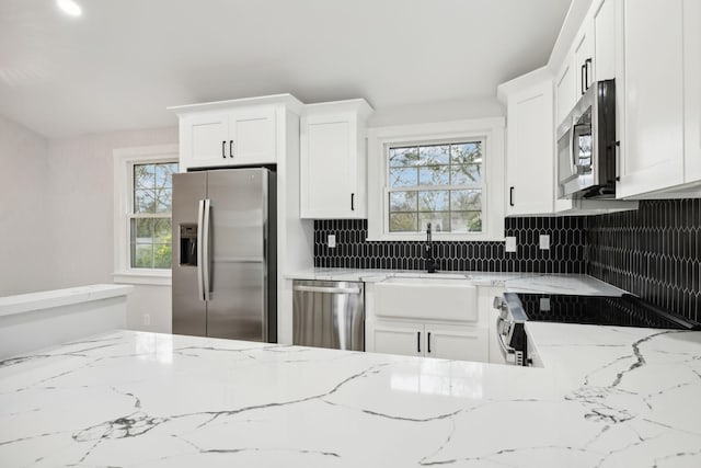 kitchen featuring white cabinets, sink, decorative backsplash, light stone countertops, and appliances with stainless steel finishes