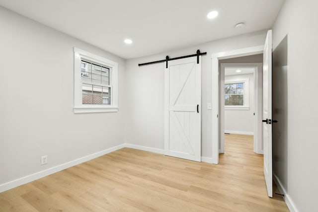 unfurnished bedroom featuring a barn door and light hardwood / wood-style floors