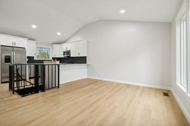 kitchen with white cabinets, vaulted ceiling, appliances with stainless steel finishes, a kitchen bar, and kitchen peninsula