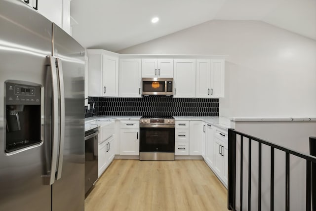 kitchen with light stone countertops, white cabinetry, appliances with stainless steel finishes, and vaulted ceiling