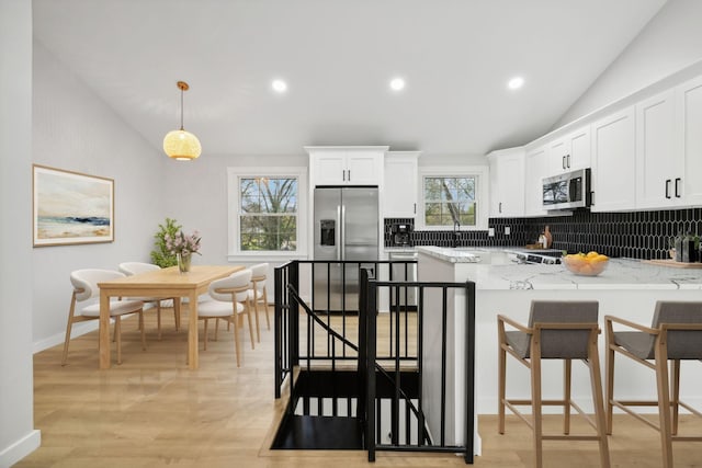 kitchen with decorative backsplash, white cabinets, decorative light fixtures, and appliances with stainless steel finishes