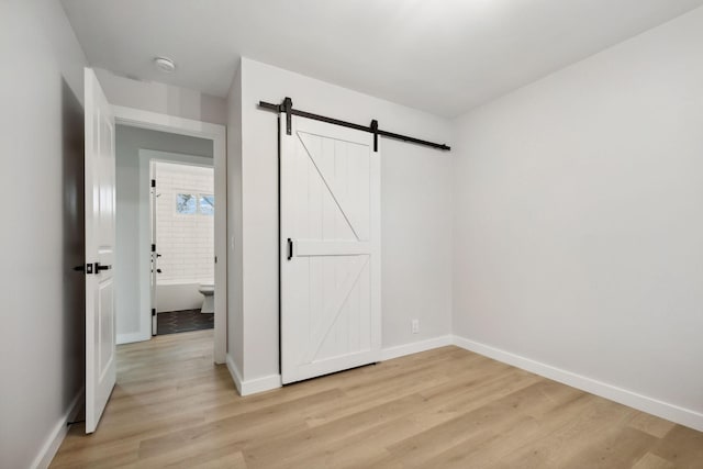 unfurnished bedroom with connected bathroom, a barn door, and light hardwood / wood-style floors