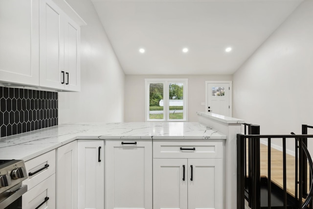 kitchen featuring white cabinets, kitchen peninsula, light stone countertops, and stainless steel range with electric cooktop