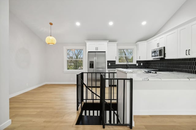 kitchen featuring light stone countertops, appliances with stainless steel finishes, decorative light fixtures, white cabinets, and lofted ceiling