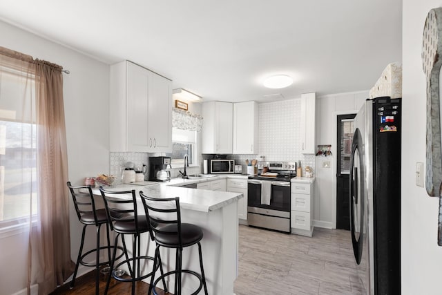 kitchen featuring kitchen peninsula, appliances with stainless steel finishes, a kitchen breakfast bar, sink, and white cabinetry