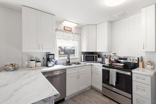 kitchen with appliances with stainless steel finishes, tasteful backsplash, sink, light hardwood / wood-style flooring, and white cabinets