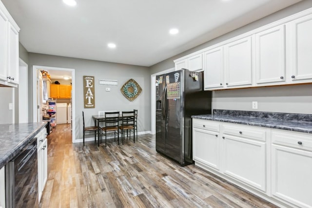 kitchen with white cabinetry, washing machine and dryer, dark stone counters, light hardwood / wood-style floors, and black appliances