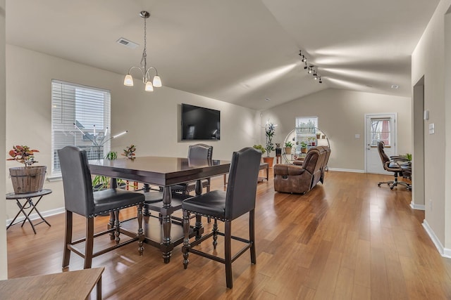 dining space with a chandelier, wood-type flooring, lofted ceiling, and track lighting