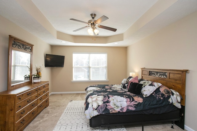 bedroom with light carpet, a raised ceiling, and ceiling fan