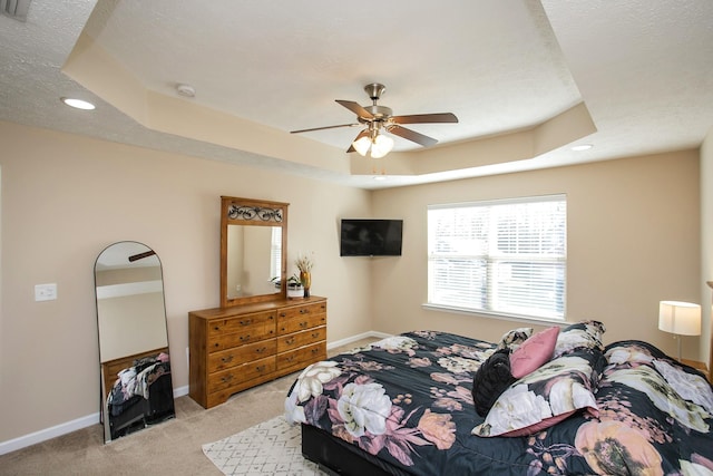 bedroom with ceiling fan, a raised ceiling, and light carpet