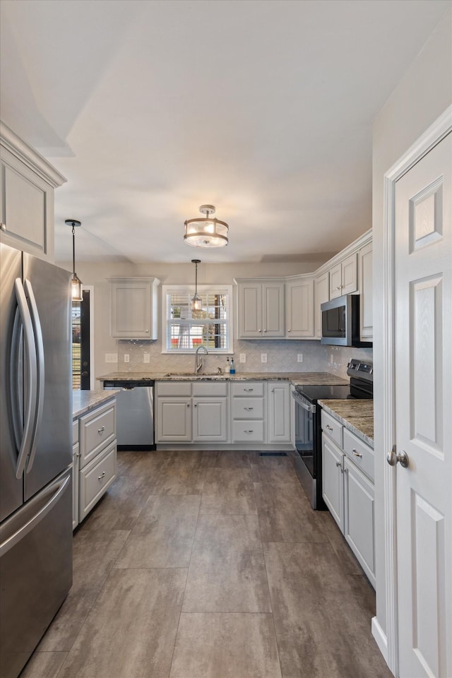 kitchen featuring light stone counters, hanging light fixtures, stainless steel appliances, tasteful backsplash, and sink