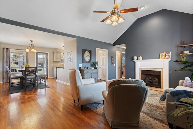 living room with ceiling fan with notable chandelier, a fireplace, light hardwood / wood-style flooring, and lofted ceiling