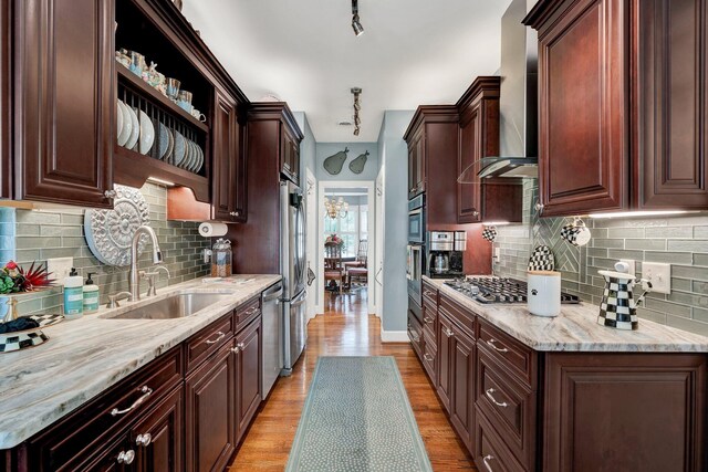 kitchen with sink, stainless steel appliances, wall chimney range hood, light hardwood / wood-style flooring, and backsplash