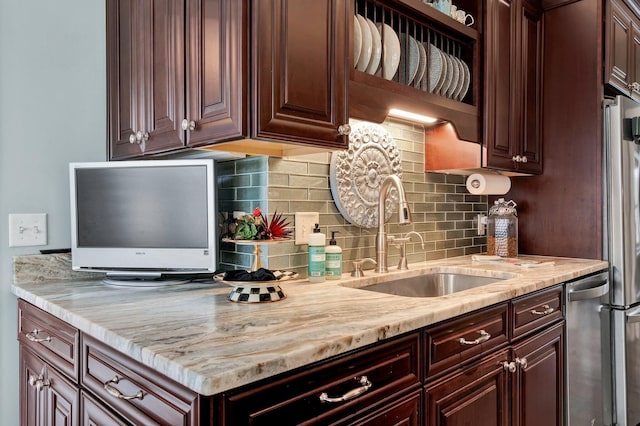 kitchen with sink, decorative backsplash, light stone counters, dark brown cabinetry, and stainless steel appliances