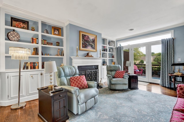 sitting room with hardwood / wood-style flooring, built in shelves, ornamental molding, and a fireplace