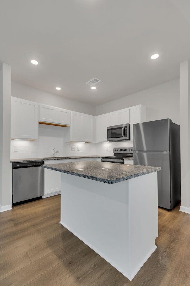 kitchen with white cabinetry, a kitchen island, stainless steel appliances, and wood-type flooring