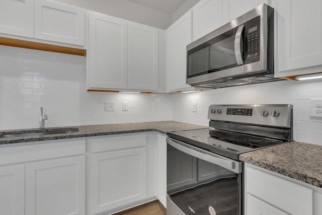 kitchen with appliances with stainless steel finishes, white cabinetry, dark stone countertops, and sink