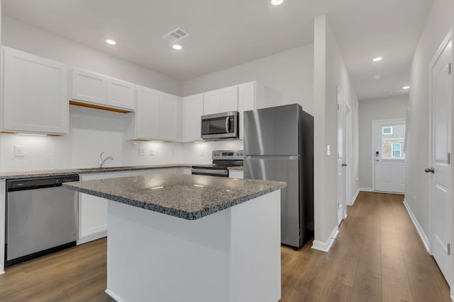 kitchen with appliances with stainless steel finishes, a kitchen island, dark stone countertops, light hardwood / wood-style floors, and white cabinetry