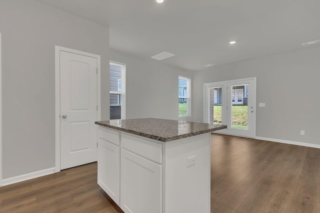 kitchen featuring white cabinets, dark hardwood / wood-style floors, a kitchen island, and dark stone counters