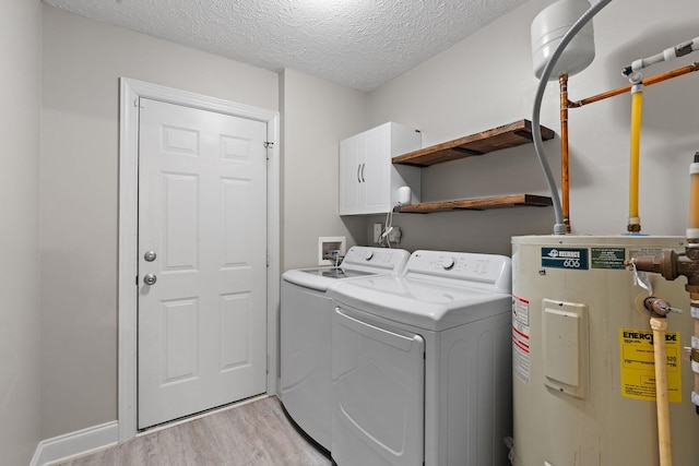 laundry room featuring washing machine and clothes dryer, cabinets, water heater, light hardwood / wood-style floors, and a textured ceiling