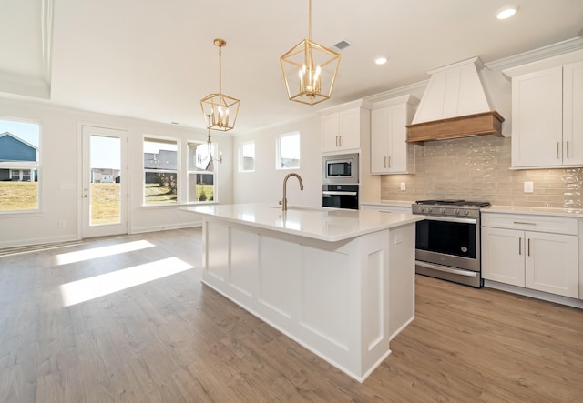 kitchen featuring custom range hood, stainless steel appliances, white cabinetry, and pendant lighting