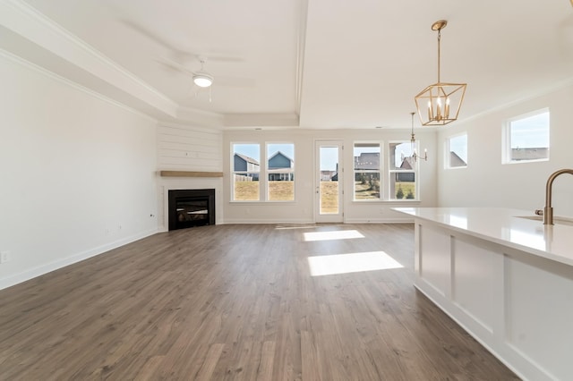 unfurnished living room with ceiling fan with notable chandelier, a tray ceiling, dark wood-type flooring, and sink