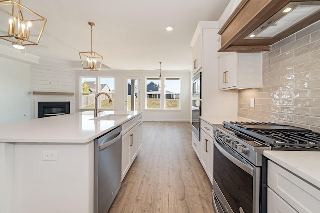 kitchen with custom exhaust hood, a center island with sink, sink, appliances with stainless steel finishes, and white cabinetry