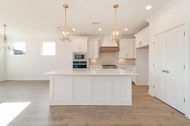 kitchen featuring an island with sink, hanging light fixtures, and custom range hood