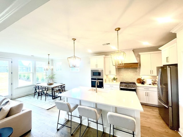 kitchen with custom range hood, stainless steel appliances, white cabinetry, and a center island with sink