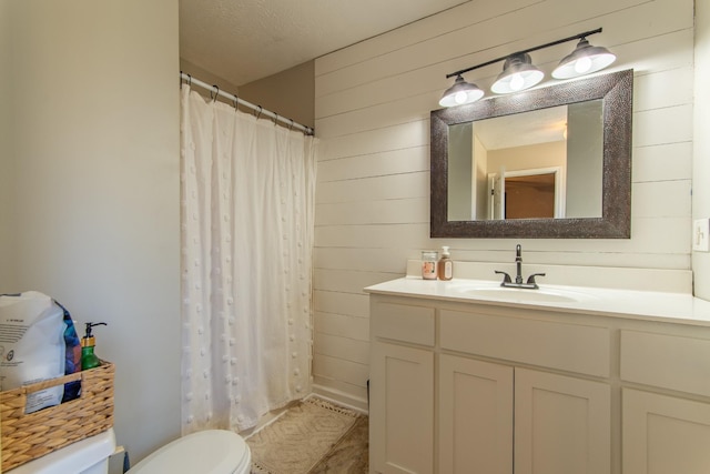 bathroom featuring wood walls, vanity, a textured ceiling, and toilet