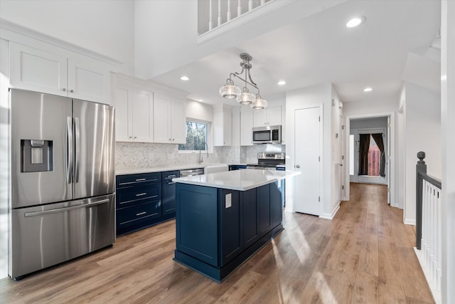 kitchen featuring stainless steel appliances, blue cabinets, pendant lighting, a center island, and white cabinetry