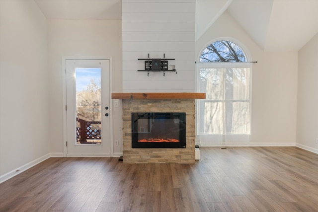 unfurnished living room featuring a stone fireplace, wood-type flooring, and vaulted ceiling